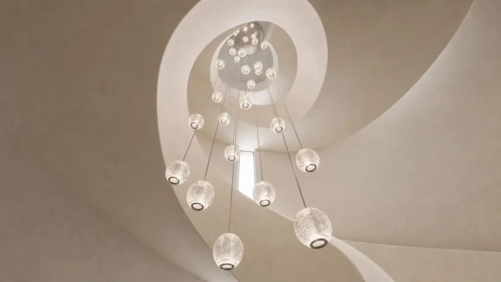 Globos de vidrio iluminados y suspendidos en una escalera curva, rodeados por bordes arquitectónicos