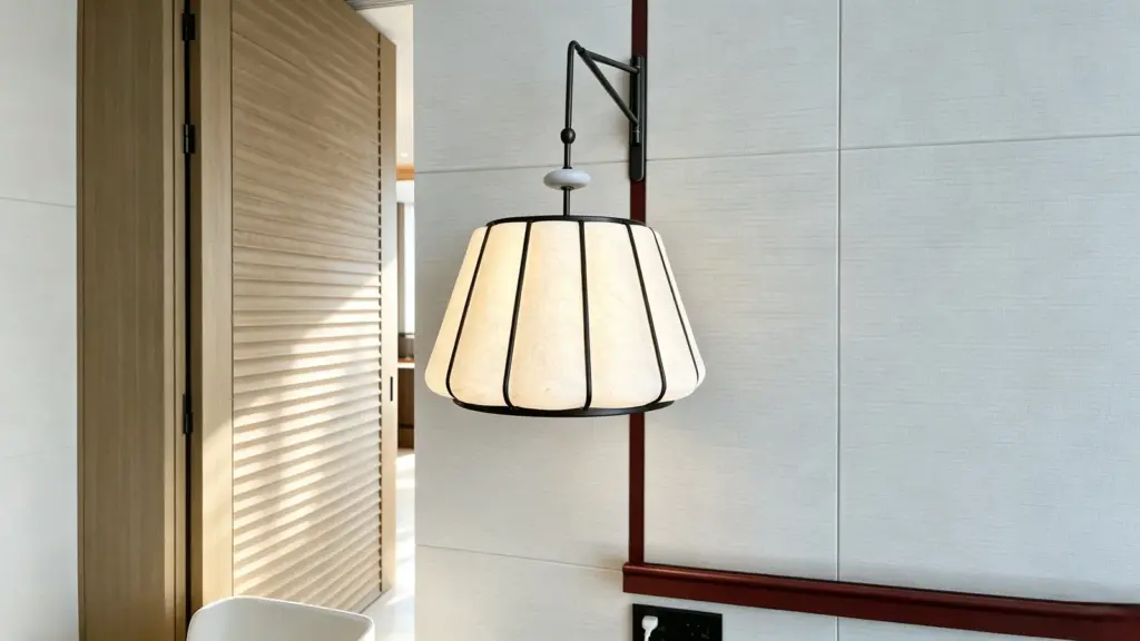 Decorative wall-mounted light with a black support arm and glowing pale shade beside a finished interior wall